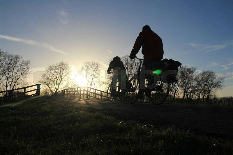 The two bikers are going home and cycling almost on the wooden bridge in the park at the country side at sunset in spring, stock photo