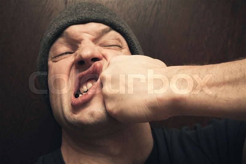 Strong fist punching the face of young angry Caucasian man, stock photo