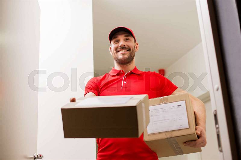 Delivery, mail, people and shipment concept - happy man in red uniform with parcel boxes at open customer door, stock photo