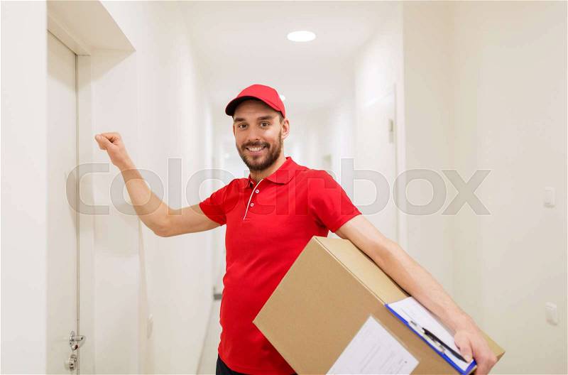 Delivery, mail, people and shipment concept - happy man in red uniform with parcel box in corridor knocking on door, stock photo