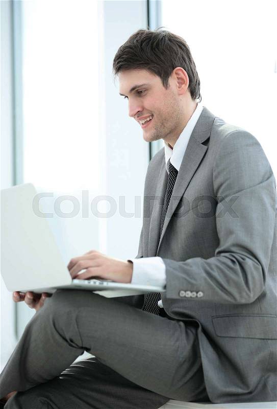 Side view: smiling student sitting on the windowsill near a large window and looks into the laptop . the photo has a empty space for your text, stock photo