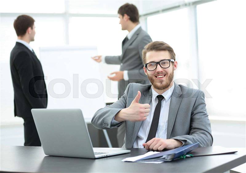 In the foreground is a successful Manager sits at a Desk before an open laptop .in the background - colleagues discussing a new presentation . in the photo there is an empty space for your text, stock photo