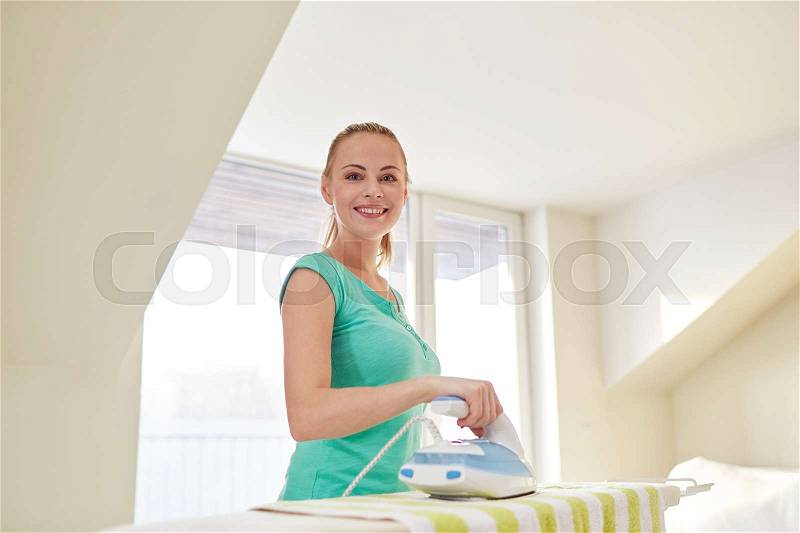 People, housework, laundry and housekeeping concept - happy woman with iron and ironing board at home, stock photo