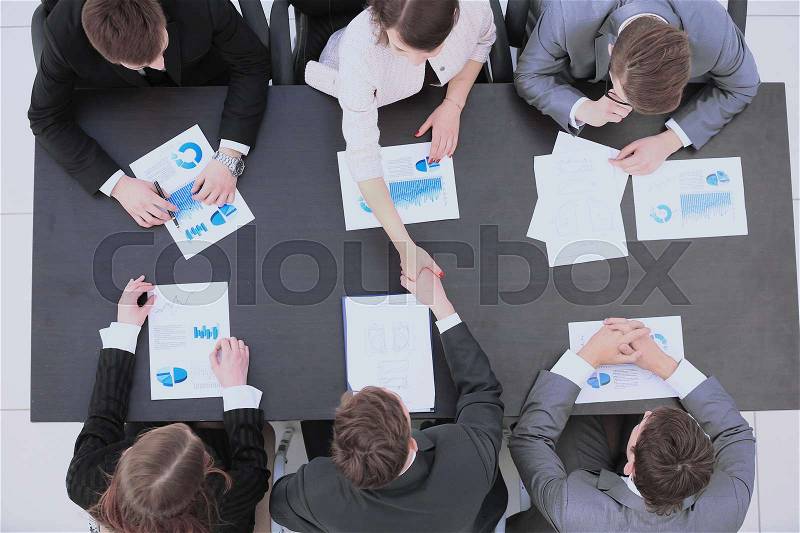Top view: accountant in two companies and business partners shake hands after a debate on the new financial plan. on the table financial charts and blank sheets, stock photo