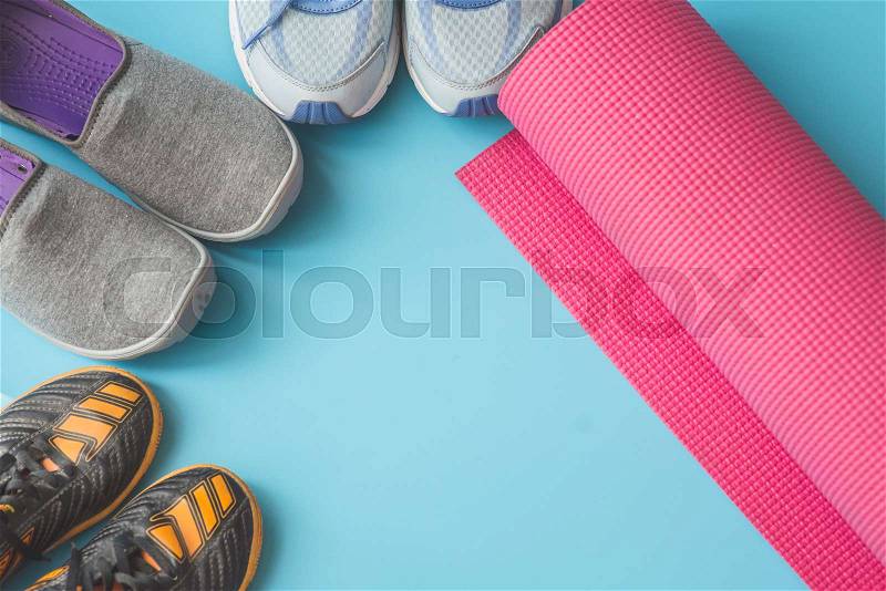 Orange, blue, and gray sport shoes with pink yoga mat on blue background, stock photo