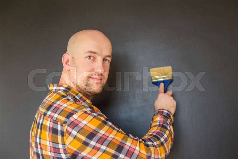 Young man painting wall with black paint, stock photo