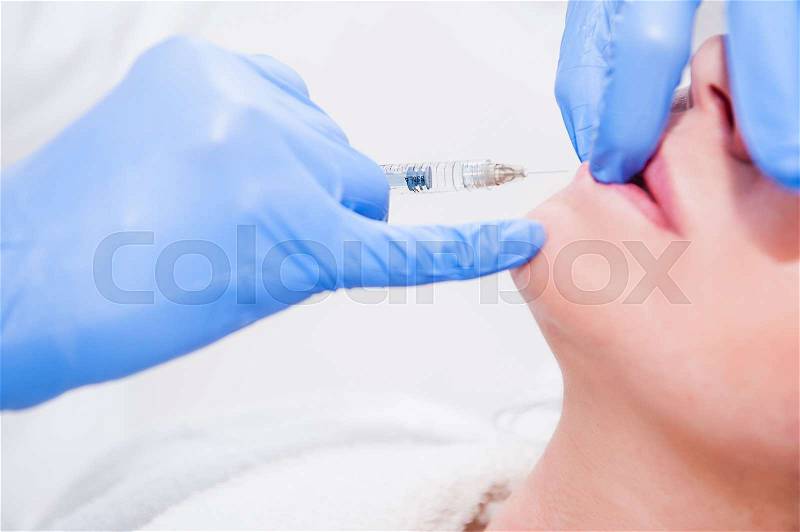 Close up Hands of cosmetologist making injection in face, lips. Young woman gets beauty facial injections in salon. Face aging, rejuvenation and hydration procedures. Aesthetic cosmetology. Selective focus, stock photo