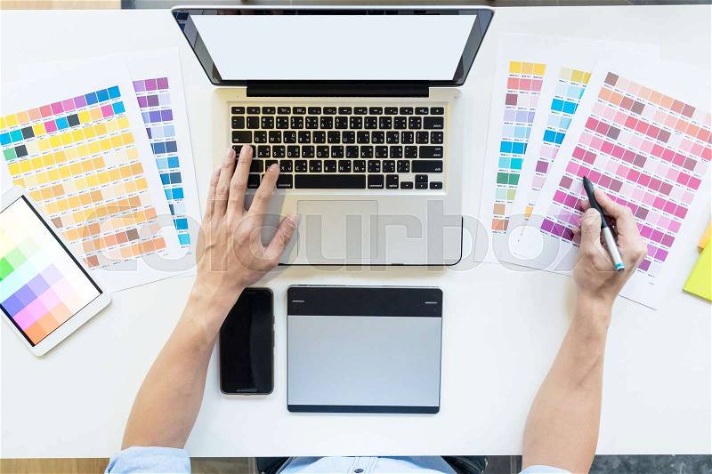 Top view of a young graphic designer working on a desktop computer and using some color swatches, top view, stock photo