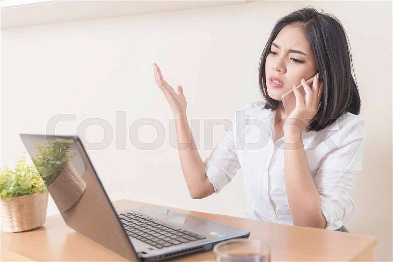 Furious businesswoman wearing suit working on line using a smart phone in a desk at office. Business problem, stock photo