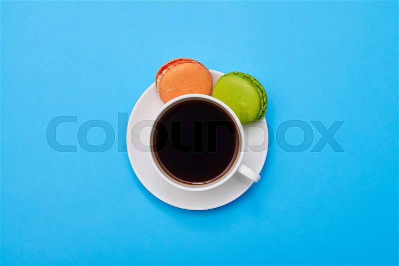Colorful macaroons with a cup of coffee isolated over blue flatlay, stock photo