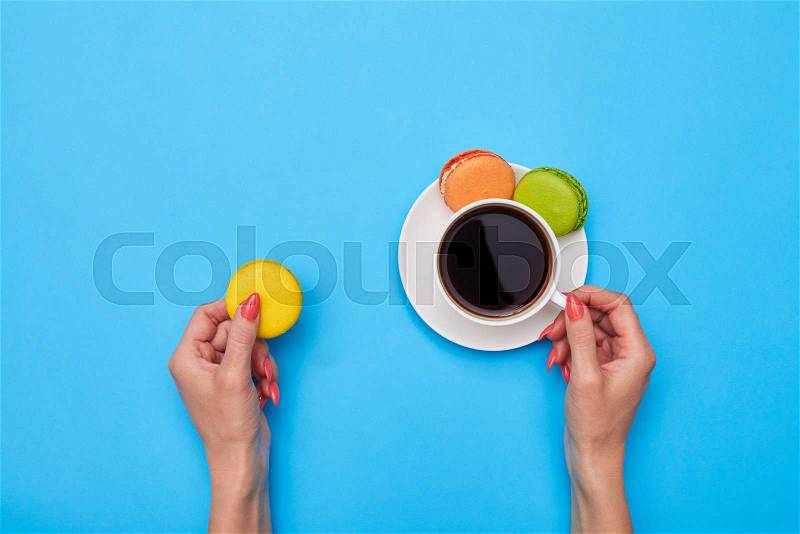 Hands holding macaroon like a perfect match for a cup of coffee on flatlay, stock photo