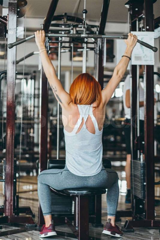 Woman training her back and shoulder with weight machine in a gym, stock photo