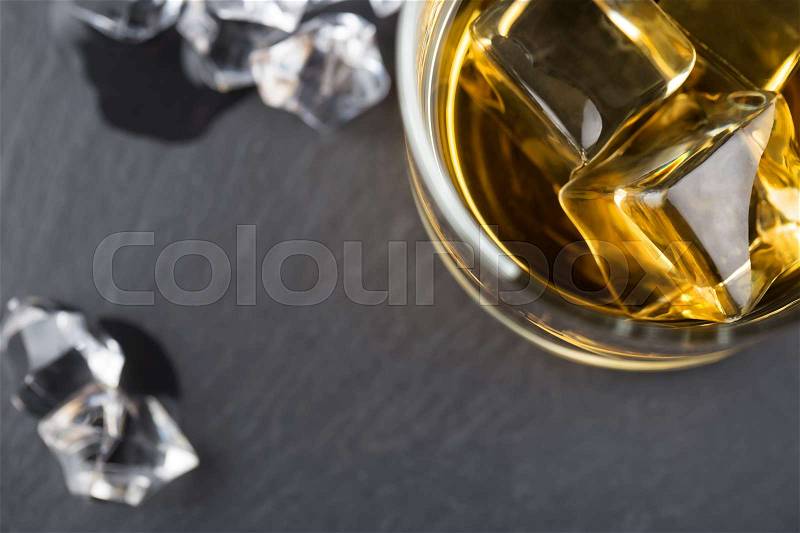 Fragment of a round glass of whiskey with ice and ice cubes on a blurry dark background, stock photo