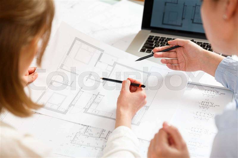 Young female architect and designer work and discuss details of a blueprint project of new apartments. Photo concept of work on technical drawings, stock photo