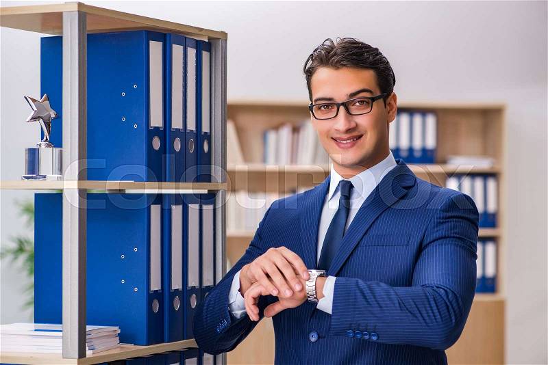 Young man standing next to the shelf with folders, stock photo