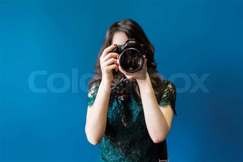 Woman takes images holding photographic camera, isolated on a dark blue, stock photo