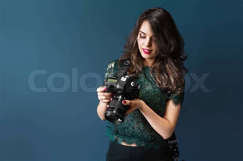 Woman takes images holding photographic camera, isolated on a dark blue, stock photo