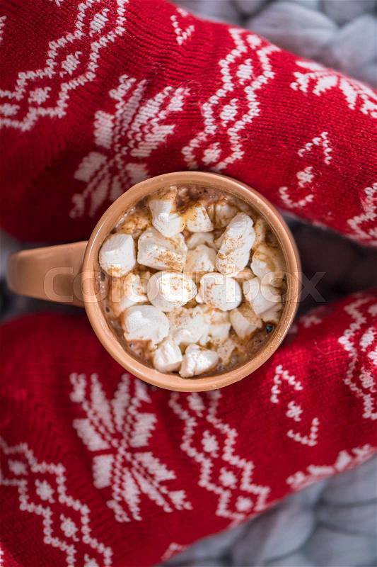 Close-up view of female feet in red knitted socks and cup with hot chocolate and marshmellows, stock photo