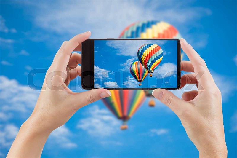 Female Hands Holding Smart Phone Displaying Photo of Blue Sky with Hot Air Balloons Behind, stock photo