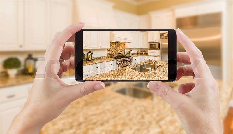 Female Hands Holding Smart Phone Displaying Photo of Kitchen Behind, stock photo
