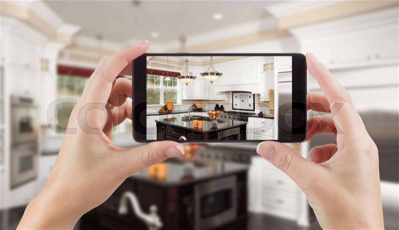 Female Hands Holding Smart Phone Displaying Photo of Kitchen Behind, stock photo