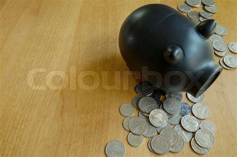 Lot of coins and black piggy bank on wood table, stock photo