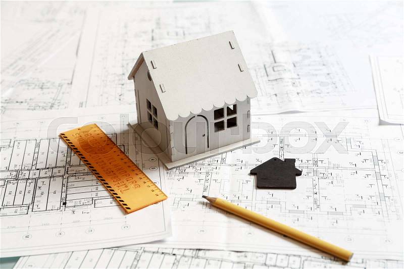 View of a white model house on top of blueprints and architect work tools, stock photo