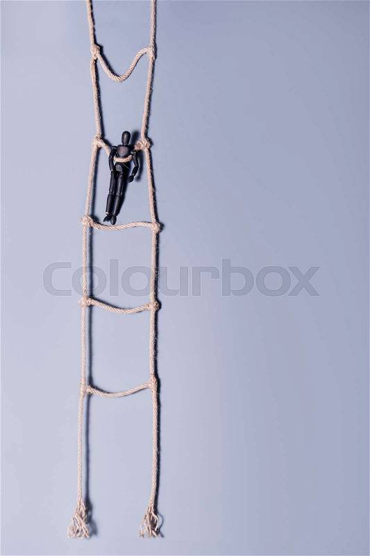 Wooden dark mannequin standing on the hanging rope ladder on the blue background. Life Concept. Selective focus, stock photo