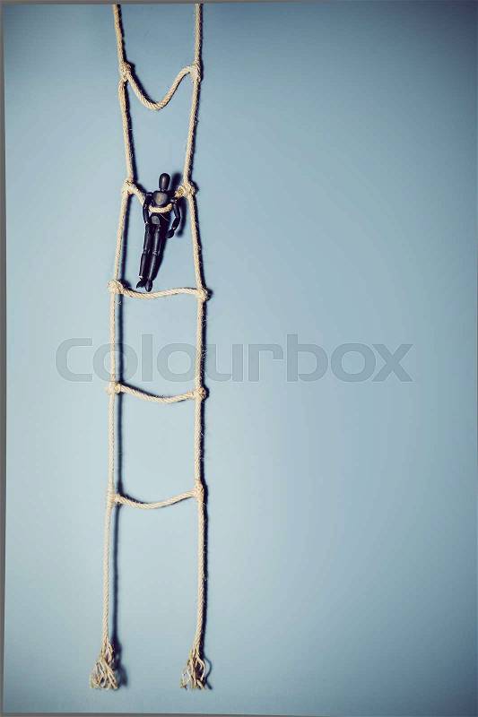 Wooden dark mannequin standing on the hanging rope ladder on the blue background. Life Concept. Selective focus, stock photo