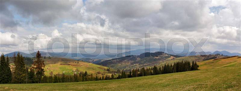 Spring mountain panorama. Clouds and sun on the hills. Spring storm. April rain. Village in the valley. April rural scene, stock photo