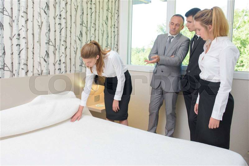 Supervisor watching hotel worker make bed, stock photo