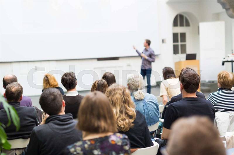 Male speaker giving presentation in lecture hall at university workshop. Audience in conference hall. Rear view of unrecognized participant. Scientific conference event. Copy space on whitescreen, stock photo