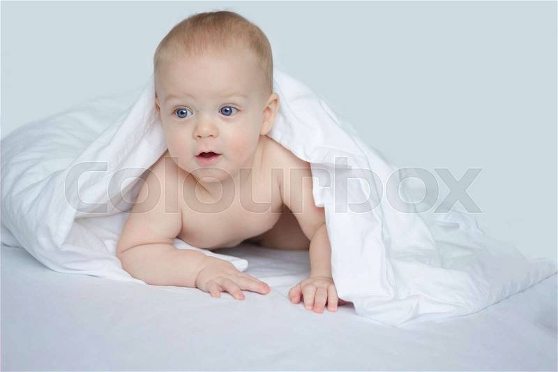 Handsome 8 month boy under white blanket on white background, stock photo