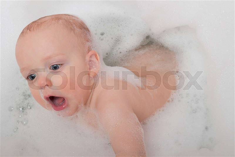 Surprised nine-month-old kid in a bathtub with soap foam, stock photo