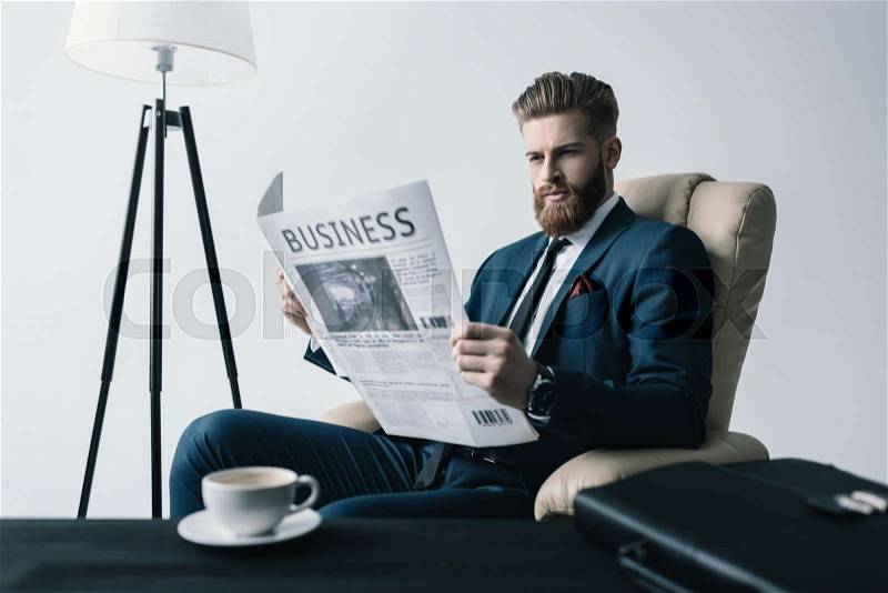 Side view of concentrated businessman reading newspaper in office, stock photo
