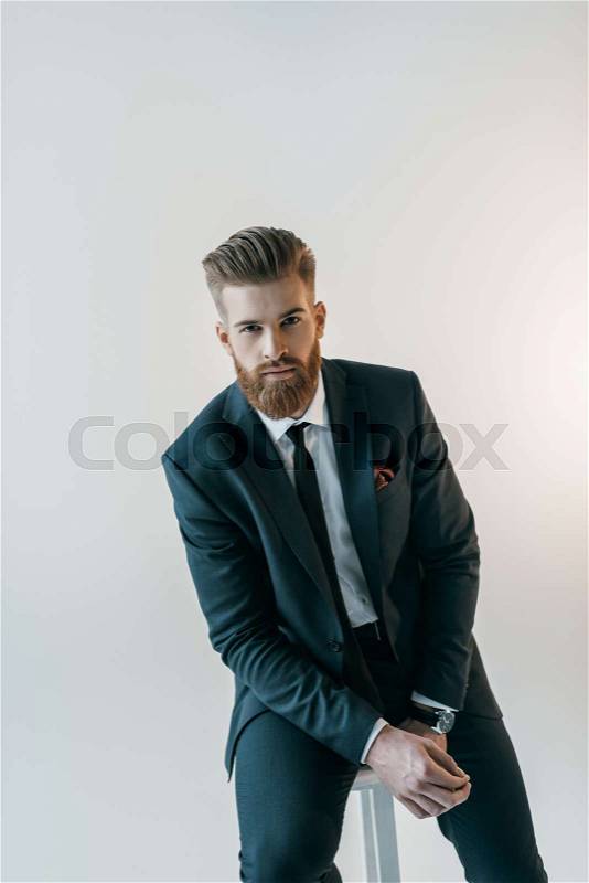 Portrait of stylish man in suit on chair on white, stock photo