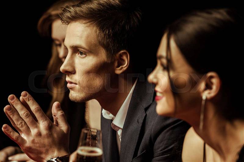 Side view of elegant young people drinking alcohol and looking away on black, stock photo
