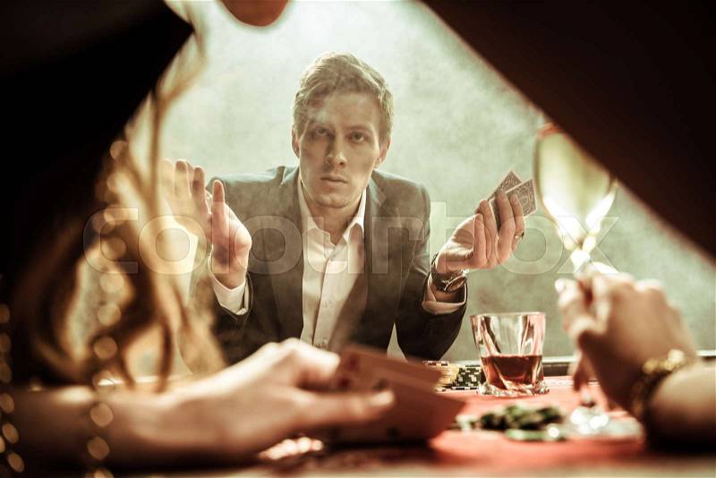 Confused man with poker cards in hand looking at woman, stock photo