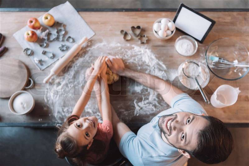 \'Top view of father and daughter kneading dough and smiling at camera, stock photo