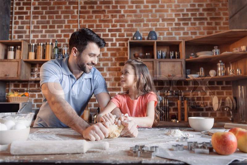 \'Happy father and daughter kneading dough and looking at each other, stock photo