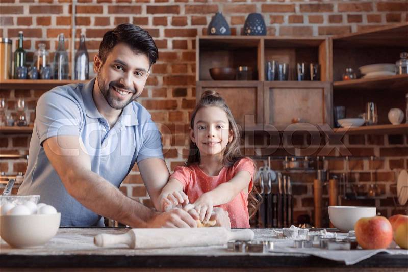 \'Happy father and daughter kneading dough and smiling at camera , stock photo
