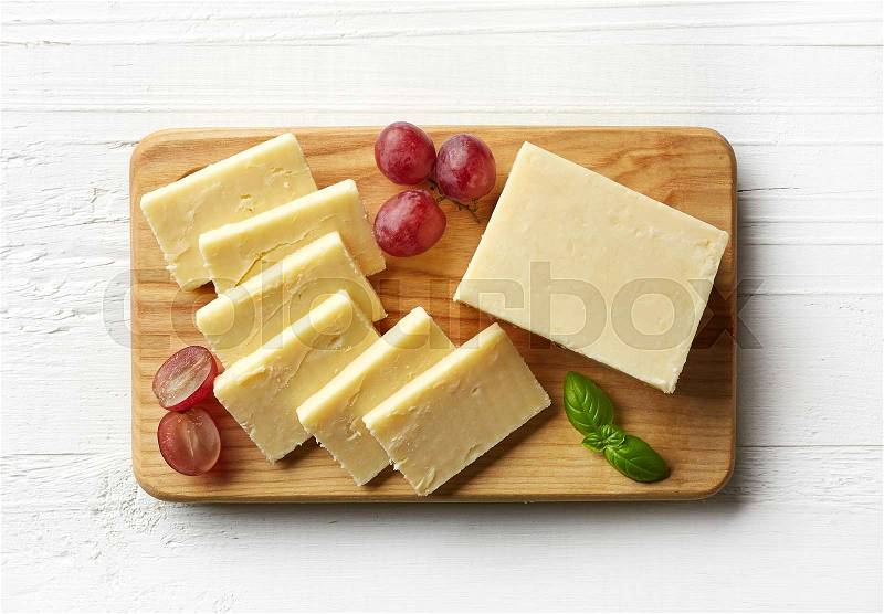 Cutting board of white cheddar cheese on white wooden background. From top view, stock photo