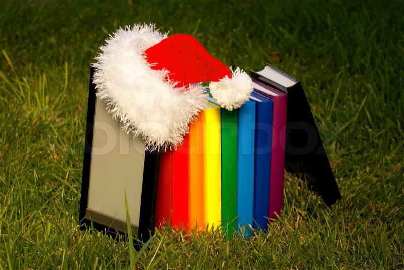 Electronic book reader wearing Santa\'s hat with row of books, stock photo