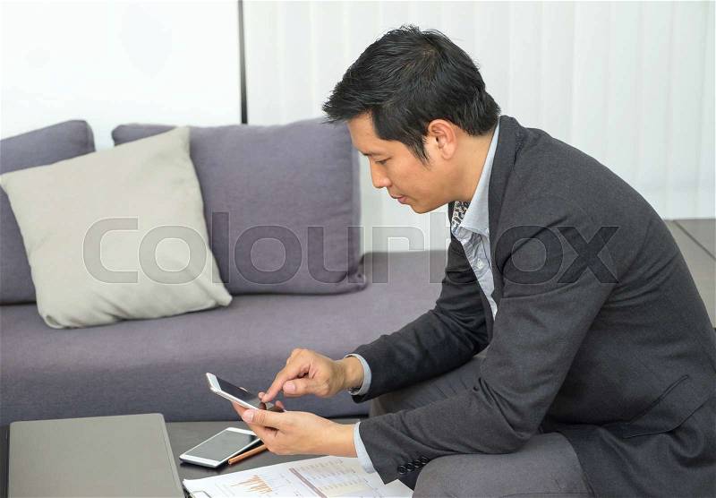 Businessman sitting at sofa and looking down at mobile phone screen at office,Feeling stress about financial crisis, stock photo