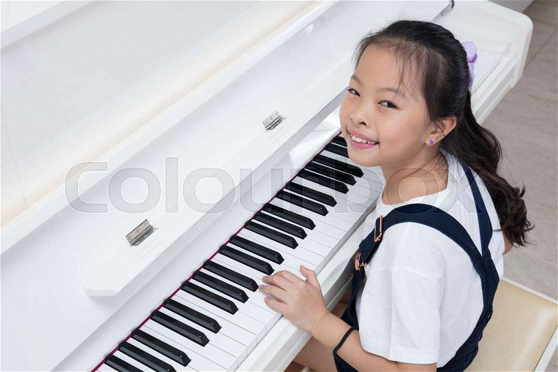 Happy Asian Chinese little girl playing classical piano in the living room at home, stock photo