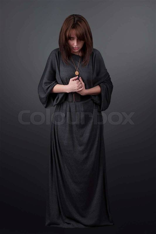 Portrait of a young caucasian woman praying. Prayer girl dressed in Vestments of a nun on gray studio background. Religion and hope concept, stock photo