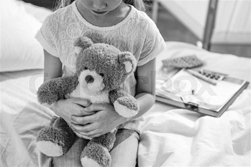 Partial view of girl with teddy bear in hospital chamber, black and white photo, stock photo