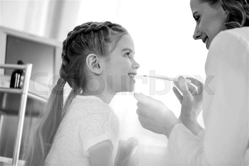 Side view of doctor measuring temperature of smiling girl, black and white photo, stock photo
