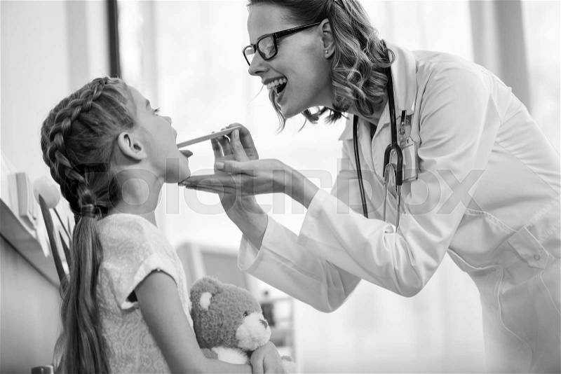 Smiling woman doctor checking throat of little girl patient, black and white photo , stock photo