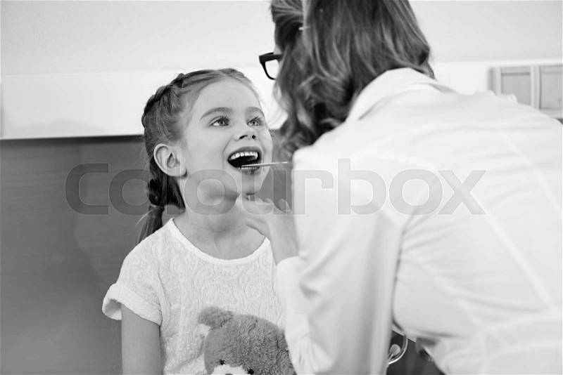 Woman doctor checking throat of smiling little girl patient, black and white photo , stock photo
